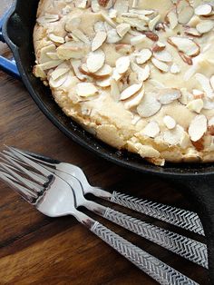 there is a pie with almonds on it and two forks in the foreground