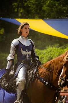 a man riding on the back of a brown horse next to a yellow and blue tent