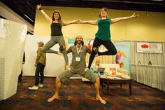 three people are doing yoga poses in an office setting with one man standing on his knees