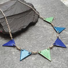 "Perfect for any fan of colourful jewellery, this bright and cheerful bunting flag necklace is the perfect choice for summer festival style this season! This enamel necklace was entirely handmade by me. I cut, drilled and smoothed the little triangles from copper sheet before enamelling them in wedgewood blue, deep blue and willow green using the torch fired enamel method. Each bunting flag has two layers of opaque colour on the front and one layer of opaque black on the back. They are strung to Summer Festival Style, Green Enamel Necklace With Large Pendant, Multicolor Enamel Pendant Necklaces, Handmade Green Enamel Necklaces, Multicolor Enamel Pendant Necklace, Handmade Artisan Enamel Necklace, Jewellery Summer, Summer Festival Fashion, Blue Bunting