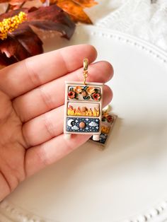 a person is holding a small pendant in their hand, with autumn leaves on the table behind them