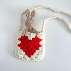 a crocheted bag with a stuffed rabbit holding a red heart in the middle