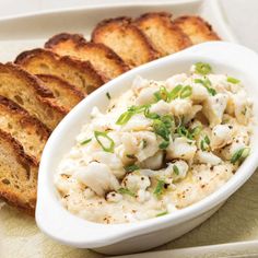 a white bowl filled with food next to slices of bread on top of a plate