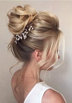 a woman with blonde hair in a messy updo wearing a white top and pearls on her head