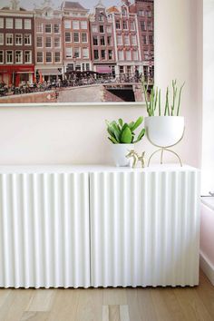 a white radiator in front of a painting on the wall next to a potted plant