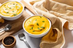 two white bowls filled with soup on top of a wooden cutting board next to spoons