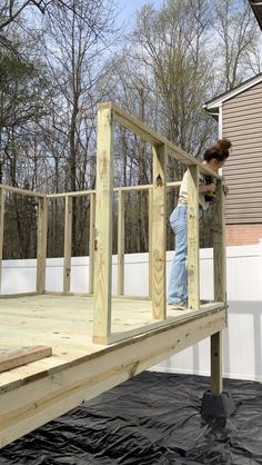 a woman standing on top of a wooden deck next to a building under construction with trees in the background