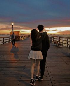 a man and woman standing on a pier next to the ocean at sunset or dawn