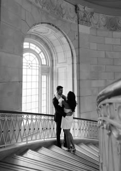 a man and woman standing on top of a staircase next to each other in front of a window