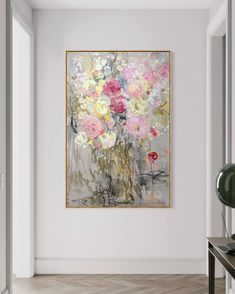 a painting hanging on the wall next to a table with a lamp and vase filled with flowers