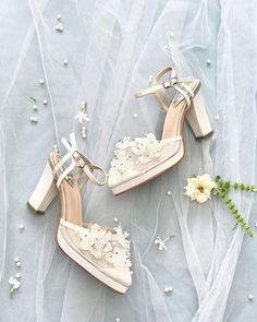 two pairs of high heeled shoes with flowers on the side and veil behind them