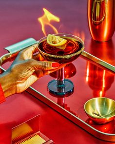 a hand holding a martini glass on top of a red table next to gold dishes