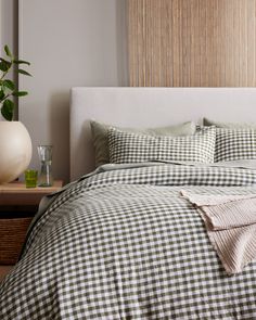 a bed with gingham checkered sheets and pillows on top of it next to a plant