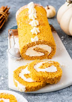 pumpkin roll with cream cheese frosting sitting on a cutting board next to other fall decorations