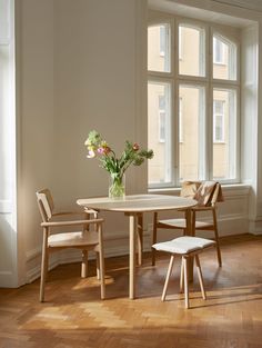 a table and chairs in front of a window with flowers on the table next to it