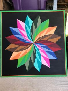 a colorful flower made out of colored paper on a black background with green trim around the edges