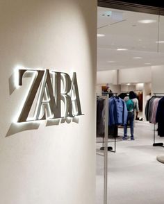 the zara logo is lit up on the wall next to clothing racks and clothes