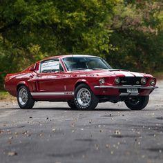 an old red car is parked on the side of the road in front of some trees