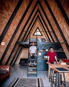 two men standing in an attic kitchen with wooden walls and beams on the ceiling,