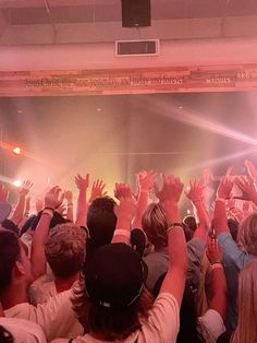 a large group of people at a concert with their hands in the air and lights on