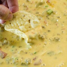 a person dipping tortilla chips into a bowl of yellow soup with broccoli and cheese