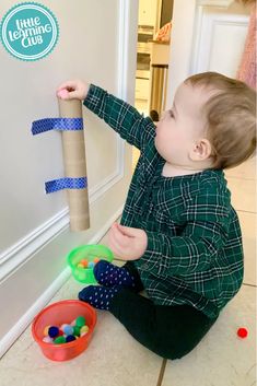 a toddler playing with a roll of toilet paper and some balls on the floor