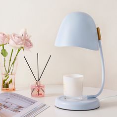 a blue lamp sitting on top of a table next to a vase with pink flowers