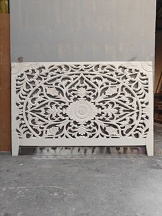 an intricately carved white headboard sits on the floor in front of a wall