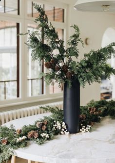 a black vase filled with pine cones and greenery on top of a white table