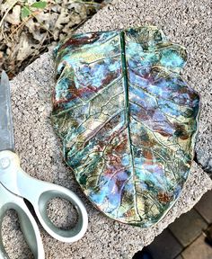 a pair of scissors sitting next to a leaf shaped tray on top of a stone slab