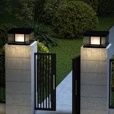 two metal gates with lights on them in the middle of a sidewalk next to bushes