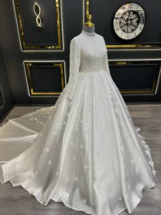 a white wedding dress on display in front of a black and gold wall with an ornate clock