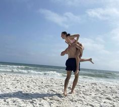 a man holding a woman on the beach while she is playing with her in the sand