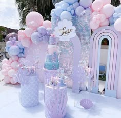 a table topped with balloons and cakes next to a wall covered in pink, blue and white