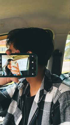 a man taking a photo with his cell phone in the back seat of a car