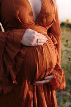 a pregnant woman in an orange dress holding her belly