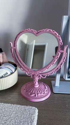 a pink vanity mirror sitting on top of a wooden table next to a white container