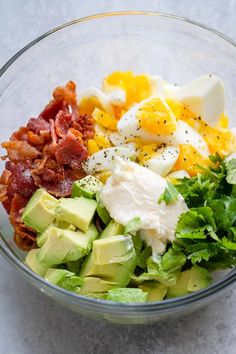 a glass bowl filled with eggs, avocado, bacon and lettuce