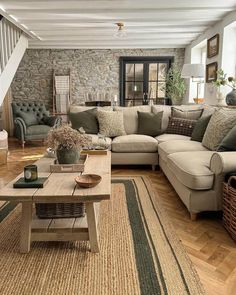 a living room filled with lots of furniture next to a stair case in front of a stone wall