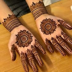 two hands with henna designs on them sitting on a wooden table next to each other