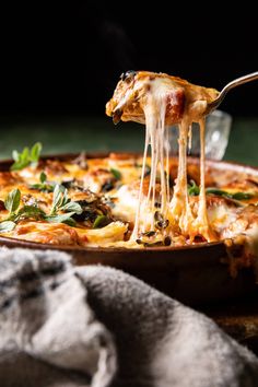 a slice of pizza being lifted with a fork from a casserole dish on a wooden table