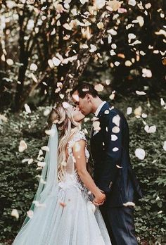 a bride and groom standing in front of trees with petals falling from the branches behind them