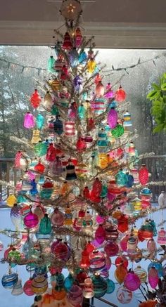 a christmas tree made out of many different colored glass ornaments in front of a window