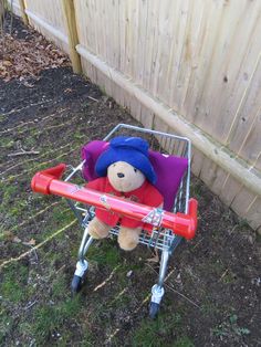 a teddy bear sitting in a red and blue stroller with purple fabric on it