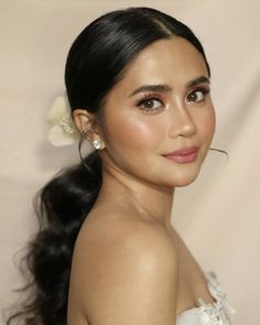 a woman with long black hair wearing a white dress and flower in her hair is looking at the camera