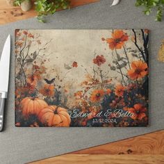 a cutting board with a knife on top of it next to some flowers and pumpkins