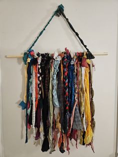 a bunch of scarves hanging on a wall next to a wooden stick with string attached