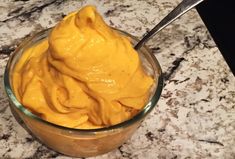 a glass bowl filled with yellow sauce on top of a marble counter next to a spoon