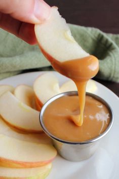 an apple slice being dipped with caramel sauce on a white plate next to sliced apples