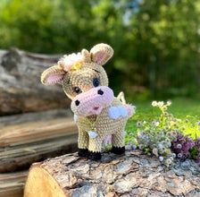 a small stuffed cow sitting on top of a tree stump next to some purple flowers